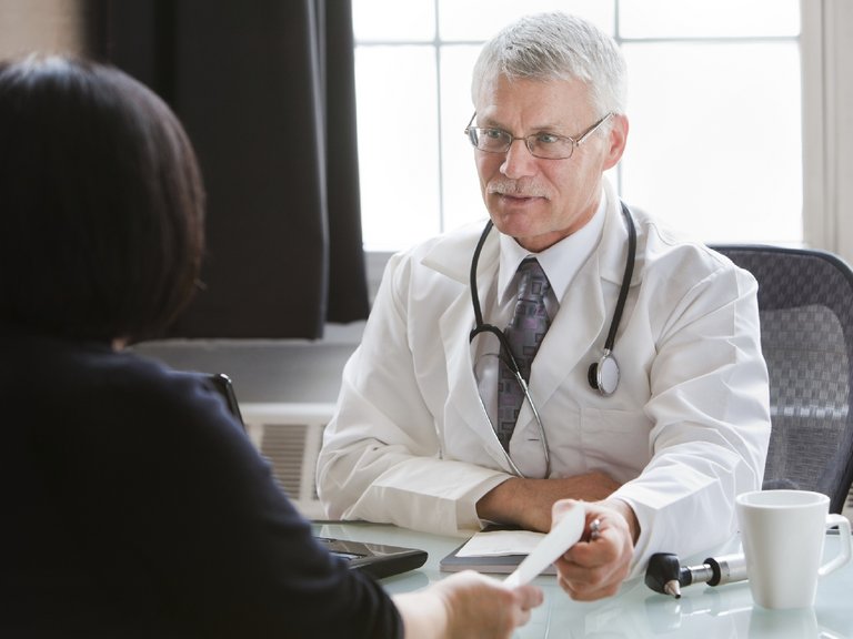 El médico le entrega una receta a la paciente