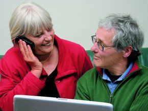 [Translate to Spain - Spanish:] Elderly couple on front f a laptop looking at each other while she is talking on the phone